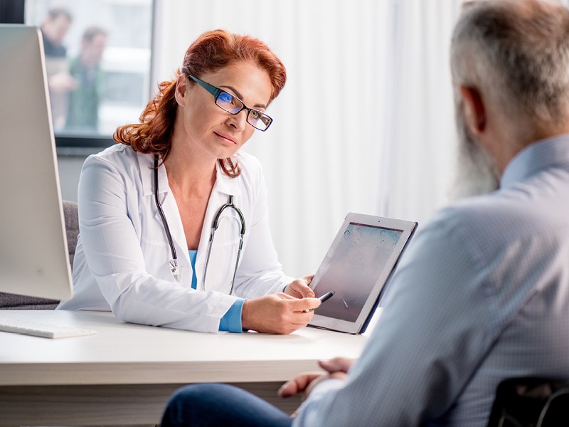 Rothaarige Ärztin mit Brille erklärt einem Patienten etwas am Tablet. © shutterstock Inc. 