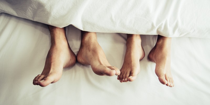 Füsse von zwei Schlafenden schauen unter der Bettdecke hervor; Foto: MiniStocker - Shutterstock.com