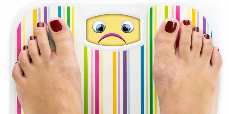 Füße auf einer Waage stehend und die Waage zeigt ein trauriges Emoji, Foto: Oko-Laa, Shutterstock.com<br />