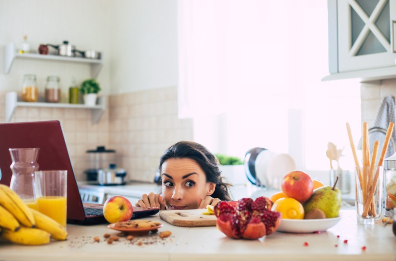 Frau, die über die Küchenarbeitsfläche linst und Obst kritisch beäugt, Foto: My-Ocean-Production, Shutterstock.com
