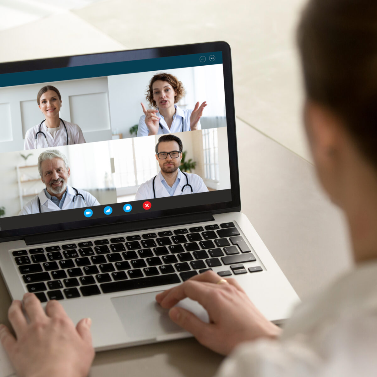 Eine Ärztin nimmt an einer Onlineschulung für Ärztinnen und Ärzte teil. Auf Ihrem Laptop sieht man vier weitere Ärzte, die auch an der Online-Schulung teilnehmen.